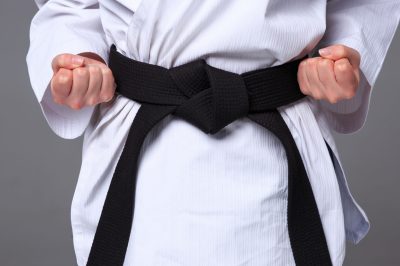 The hands of karate girl in white kimono and black belt training karate over gray background.